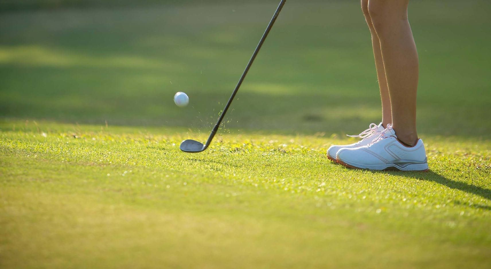 Taco de golfe logo depois da tacada, com a bola no ar sobre o gramado